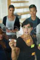 Brainstorming, diverse and creative team writing a strategy idea on sticky notes and creating a schedule on a glass board. Group using teamwork, planning and collaboration in a marketing meeting