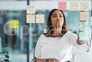 Building the best plans. a young businesswoman using a digital tablet while brainstorming with notes on a glass wall in an office.