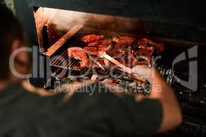 Hes on barbecuing duties. Closeup shot of an unrecognisable man grilling meat while having a barbecue.