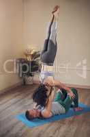 Life is a balancing act. Full length shot of a handsome young man doing acro yoga with his partner in a yoga studio.