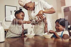 Mommy please add more. a young mother preparing cereal for her two adorable young daughters at home.