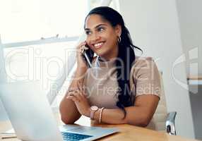 I am always connecting with clients. an attractive young businesswoman sitting and using her cellphone while working on a laptop in the office.