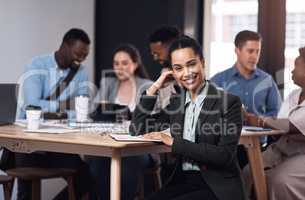 Feeling confident in her career. Portrait of a young businesswoman sitting in an office with her colleagues in the background.