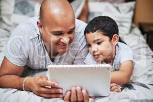 I wonder what will happen next. a cheerful young man and his son watching videos on a digital tablet together while hanging out on a bed at home during the day.