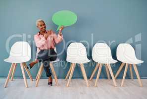 Check this out guys. Studio portrait of an attractive young businesswoman pointing to a speech bubble while siting in line against a grey background.