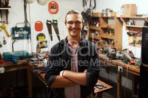 A job well done. Portrait of a confident young male carpenter standing with his arms folded inside of his workshop at night.