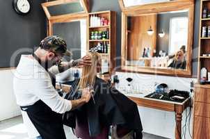 Just trimming off the edges. a male hairdresser styling a womans hair inside a salon.