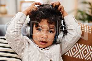 Im having a jam packed day. Portrait of an adorable little boy listening to music on headphones while sitting on a sofa at home.