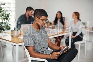 Engaged with the world online. a young businessman using a digital tablet in an office with his colleagues in the background.