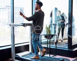 Taking the steps and making the calls to success. a young businessman talking on a cellphone and going through paperwork while walking on a treadmill in an office.