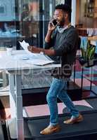 Working in a healthy and happy environment. a young businessman talking on a cellphone and going through paperwork while walking on a treadmill in an office.