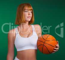 Master your body. an attractive young sportswoman standing alone and holding a basketball against a green background in the studio.
