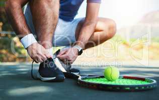 Laced up and ready to do battle. an unrecognizable male tennis player tying his shoelaces outdoors on a tennis court.