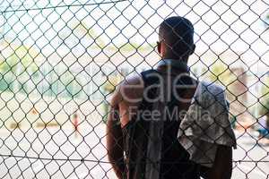 Look in the mirror - thats your competition. Rearview shot of a sporty young man taking a break while standing against a fence on a sports court.