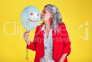 Dont just count your years, make your years count. a funky and stylish senior woman kissing a balloon against a yellow background.