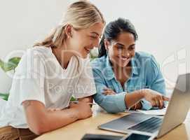 Look at this. two attractive businesswoman sitting together and using a laptop in the office.