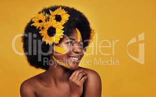 She makes sunflowers look even more aesthetic. Studio shot of a beautiful young woman smiling while posing with sunflowers in her hair against a mustard background.