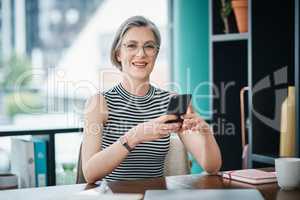 I can see how having a online presence benefits my business. a mature businesswoman using her cellphone while sitting at her desk.