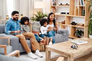 Watching movies is a family activity. Full length shot of a beautiful young family sitting on sofa and watching tv together at home.