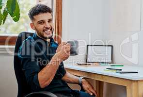 A job well done deserves a good cup of coffee. a young businessman having a coffee break at his desk in a modern office.