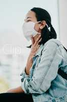 A sore throat is a common symptom of Covid-19. a young woman wearing a mask and suffering from throat pain in a doctors office.
