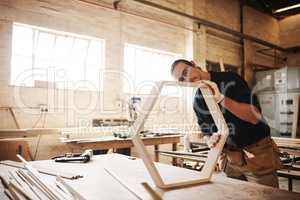 Attention to detail is pivotal in this industry. a handsome young carpenter working on a wooden frame inside a workshop.