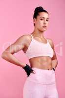 Getting fitter and fiercer by the day. Studio portrait of a sporty young woman posing with her hands on her hips against a pink background.