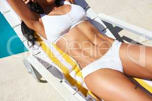 Getting her tan on. a fit young woman relaxing on a lounger.