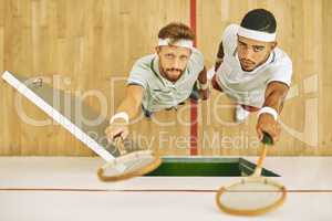 No matter the outcome carry yourself with confidence. High angle shot of two young men holding up their rackets at a squash court.