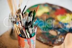 Its time to be creative. a tin full of paintbrushes in an empty art studio after a painting class.