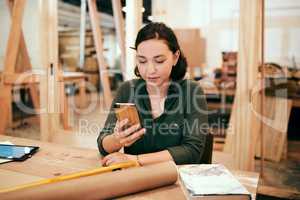 We get so many clients through social media. a female carpenter using her cellphone while sitting in her workshop.