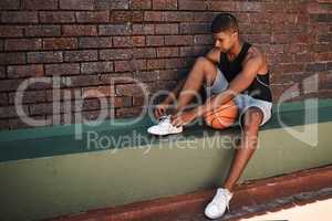 The harder you work, the harder it is to lose. a sporty young man tying his laces while playing basketball outdoors.