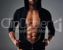 Hes got abs of steel. an unrecognizable muscular young man posing in a zipped down hoodie against a grey background.