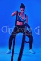 Shes in beast mode. Full length shot of an attractive young sportswoman working out with battle ropes against a blue background.