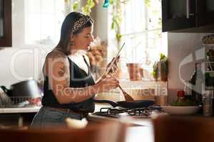 No cookbook, no problem. a young woman using a digital tablet while preparing a meal at home.