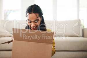 This is the best. an attractive young businesswoman sitting alone on her living room floor and opening up a mystery box.