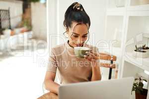 Life begins after coffee. an attractive young businesswoman sitting and enjoying a cup of coffee while using her laptop at home.