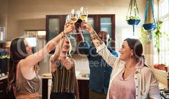Raise your glasses. a group of cheerful young friends having a celebratory toast with drinks while standing in the kitchen preparing food at home.