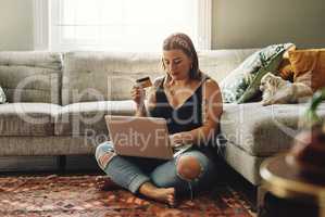 I think its time to top up on dog food. a young woman using a laptop and credit card in her living room at home.