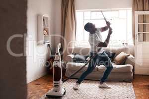 Why not have fun with chores. a young man dancing while busy vacuuming the living room.