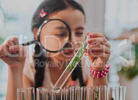 Shes learning something new about plants today. an adorable little girl looking through a magnifying glass while analysing plants from a test tube at home.
