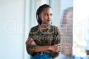 Every business started with just an idea. an attractive young businesswoman looking contemplative while standing with her arms folded in her office alone.