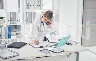 Do you mind repeating that. an attractive young female doctor writing on a clipboard while taking a phonecall in her office.
