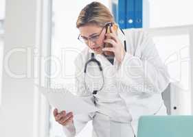 I think I have that document right here. an attractive young female doctor looking at a document while taking a phonecall in her office.