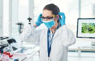 Safety first. an unrecognizable young female scientist putting on a protective face mask inside of a laboratory during the day.