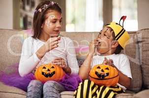 Dont eat it all at once. a young brother and sister eating their Halloween candy while sitting on their sofa at home.