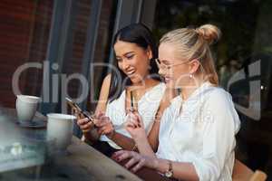 Forget waiting on a bill, just pay online. a woman using a cellphone while her friend holds up a credit card while sitting together.