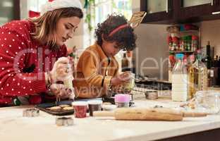 Adding some more sweet things to the cookies. a cheerful young woman and her son baking cookies together in the kitchen during christmas time at home.