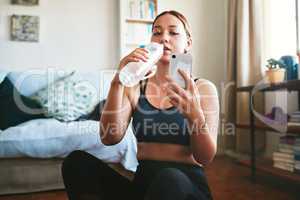 Quick water and social media break. an attractive young woman sitting and drinking water while using her cellphone after a workout.