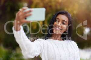 Go ahead and change the world with your smile. a young woman taking a selfie while out in the city.